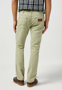 Pantalones de algodón color verde claro con un corte recto, cinco bolsillos y un parche de cuero con el logo en la parte posterior, combinados con zapatos marrones.
