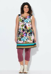 Bezrukávová květinová tunika ve živých barvách s pruhovaným lemem, spárovaná s burgundskými capri legínami a světlými vysokými botami.