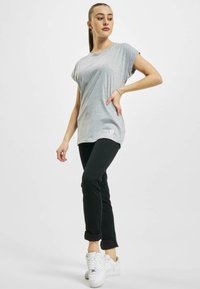 T-shirt grigio chiaro a maniche corte con orlo arrotondato, abbinato a pantaloni neri aderenti e sneakers bianche, con un discreto dettaglio del logo.