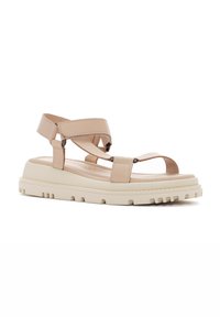 Des sandales en cuir beige présentent des sangles croisées réglables, une semelle épaisse crème avec des rainures texturées et un matelas de pied rembourré pour le confort.