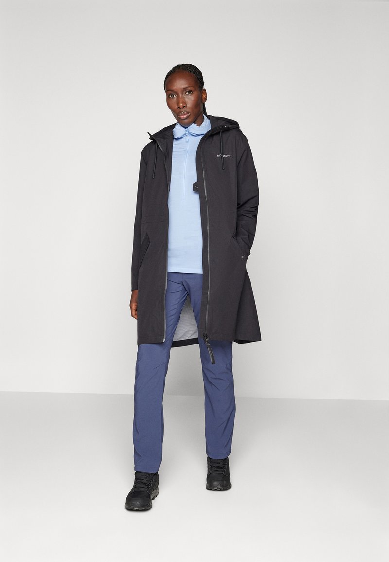 Wasserdichte schwarze Parka mit Kapuze, ausgestattet mit einem Reißverschluss vorne und Seitentaschen, kombiniert mit einem hellblauen Langarmoberteil und blauen Hosen.