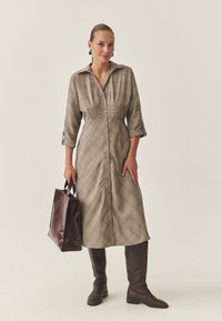 Lungo vestito a quadri con scollo con colletto, bottoni sul davanti e maniche a tre quarti. Stivali marrone scuro in pelle al ginocchio e borsa lucida color bordeaux.