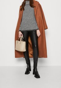 Bruine oversized jas, grijs gestreept sweater, zwarte leren legging, zwarte haklaarzen en een beige handtas. Gestructureerde materialen en een strakke vormgeving.