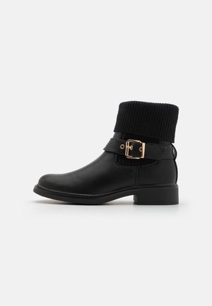 Bottine noire avec un col en tricot texturé, détails de boucle en matériel doré, finition en cuir lisse et petit talon bloc.