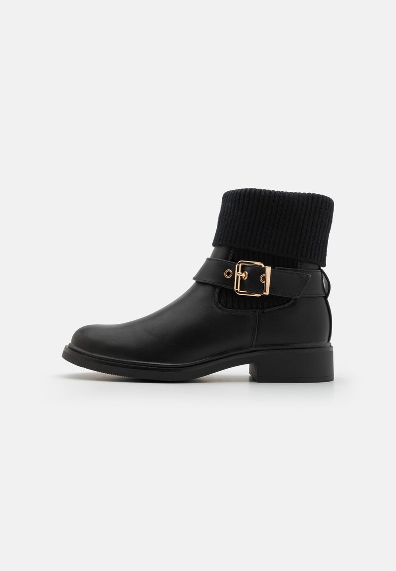 Bota preta de tornozelo com um colarinho de malha texturizada, detalhes em fivela de hardware dourado, acabamento em couro liso e um salto bloco baixo.