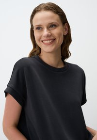 Czarny T-shirt z krótkim rękawem wykonany z miękkiego materiału, z okrągłym dekoltem i podwiniętymi rękawami, o gładkiej fakturze i luźnym kroju.