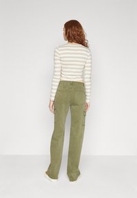 Tricou cu mâneci lungi, în dungi, în nuanțe de bej și alb, asortat cu pantaloni cargo verzi măslinii, prevăzuți cu buzunare laterale și o croială lejeră.