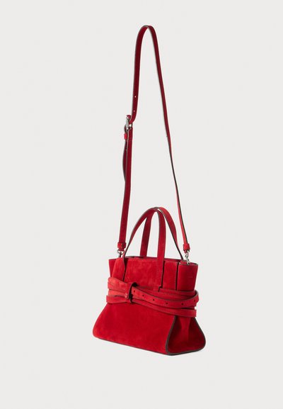 Röd mockaväska med en strukturerad design, korta handtag och ett avtagbart axelband. Har en bältesliknande accent och kontrasterande sömmar.