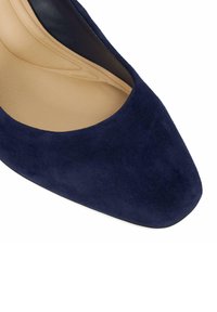 Escarpin en daim marine avec un bout pointu, doublure intérieure lisse et un design minimaliste. La semelle est élégante et plate avec une texture subtile.