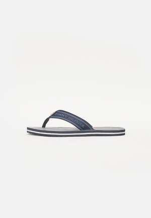 Sininen flip-flop, jossa on teksturoitu hihna, valkoinen logo ja raidallinen pohja. Kevyt, teksturoitu ulkopohja tarjoaa hyvän pidon.