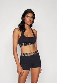 Conjunto de soutien desportivo e calções pretos com padrão dourado de clave grega ao longo da cintura, feitos de um material elástico e macio.