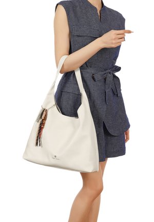 Donna con abito azzurro senza maniche che tiene una grande borsa bianca da spalla con nappine decorative.