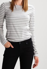 Maglia a maniche lunghe a righe grigie e bianche realizzata in tessuto morbido, abbinata a pantaloni neri con un bottone in vita.