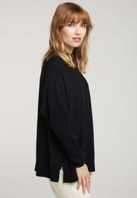 Sweater noir surdimensionné avec un ourlet côtelé, des manches longues et une finition texturée, doté d'un col rond et d'entailles sur les côtés pour le confort.
