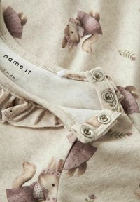 Tuta in tessuto beige con illustrazioni di conigli in abiti rosa. Chiusura a bottoni a pressione sul colletto con rifiniture a volant. Adatta per neonati di 1-2 mesi.