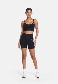 Crni sportski crop top i šorts visokog struka od glatkog materijala, s minimalnim bijelim logotipom.