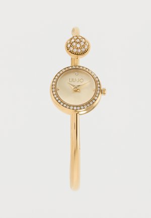 Reloj de pulsera Liu Jo tono dorado con bisel incrustado de cristales y charm redondo decorativo, esfera beige y marcadores de hora minimalistas.