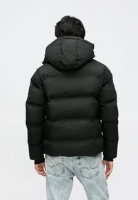 Must tikitud kapuutsiga puffer-jakk, millel on pehme tekstuur. Kandetud helesiniste teksapükstega, mis näitavad lõdvestunud istuvust.