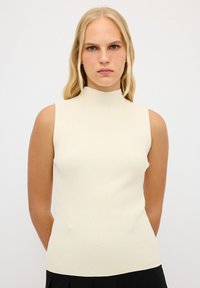Lichtbeige geribbelde mouwloze top met een hoge halslijn, voorzien van subtiele sprankelingen door de stof voor extra textuur en detail.