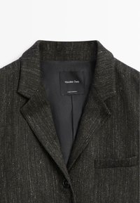 Donkergrijze blazer met een subtiele glans, gemaakt van gestructureerde stof. Bevat een opstaande kraag, één knop en een zakje op de linkerborst.