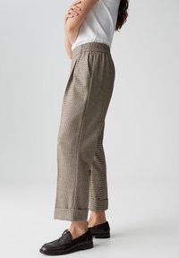Beige geruite broeken met een ontspannen pasvorm, elastische tailleband en opgerolde pijpen, gecombineerd met donkere loafers.