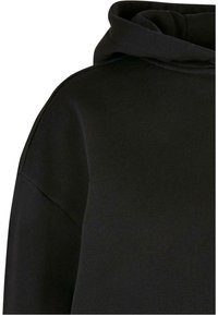 Sweat à capuche noir avec une coupe ample, une couture visible à l'épaule et une texture de tissu douce et épaisse.