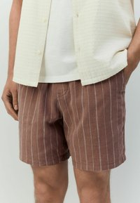 Bruine gestreepte short van lichtgewicht stof, met verticale witte strepen en een relaxte pasvorm, gecombineerd met een textuur crème shirt.