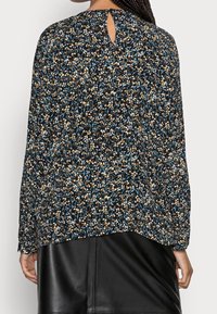 Luftige Bluse mit einem dunklen Blumenmuster in Blau, Orange und Weiß und einem schlüssellochförmigen Detail auf der Rückseite. Lange Ärmel, lockere Passform.