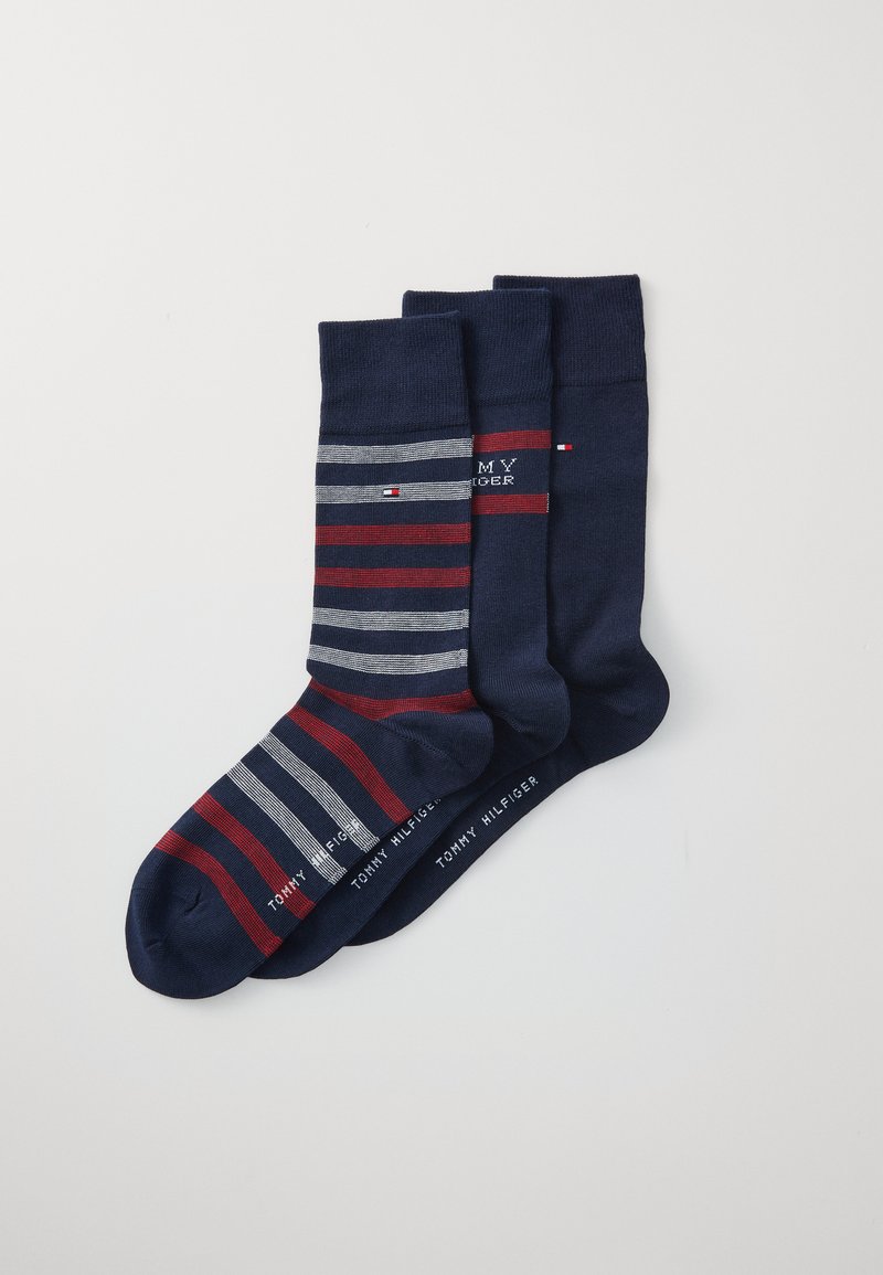 Ensemble de trois paires de chaussettes de couleur bleu marine avec des rayures rouges et grises. Le logo "TOMMY HILFIGER" apparaît sur les chaussettes. Texture en tricot lisse.
