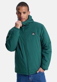 Groene geïsoleerde jas met een capuchon, voorzien van een ritssluiting, elastische manchetten en een logopatch op de borst. Soepele textuur, casual pasvorm.