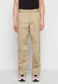 Bežové kalhoty rovného střihu vyrobené z bavlněné směsi s poutky na opasek a plochým předním dílem. Nosené s černými a růžovými teniskami.