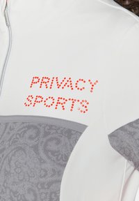 Witte sportjacket met grijze geprinte accenten, met "PRIVACY SPORTS" in rode rhinestones op de borst. Zichtbaar ritsdetail.