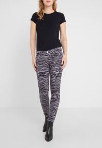 Camiseta negra de manga corta combinada con pantalones ajustados con un patrón de cebra en gris y negro, complementados con botas negras hasta el tobillo.