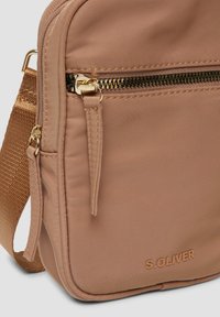 Borsa a tracolla in nylon rosa chiaro con zip dorata, tracolla regolabile e logo in rilievo sul davanti; presenta una superficie testurizzata.