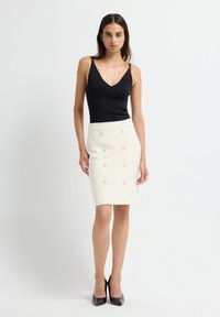 Zwarte fitted tanktop met dunne bandjes, gecombineerd met een crème-kleurige pencil skirt met grote decoratieve knopen. Geweven stof met een gladde afwerking.