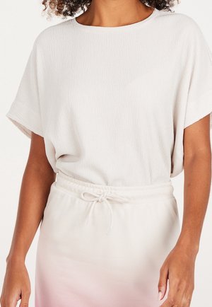 Kobieta ubrana w teksturowany biały top z krótkim rękawem włożony do białej spódnicy z troczkiem, widziana od szyi do połowy uda.