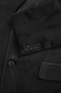 Mustast sametist bleiser, millel on sile tekstuur, neli sobiva värviga nuppu ja küljetasku. Disain sisaldab kohandatud revääre ja õmbluse detaile.