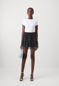 Tricou alb din bumbac, asortat cu o fustă din tul negru stratificată. Modelul ține o geantă de mână bleu deschis și poartă sandale argintii cu curea.