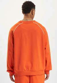Orange sweatshirt featuring a crew neck, long sleeves, and white accent stitching along the shoulder seams. Soft, textured fabric.