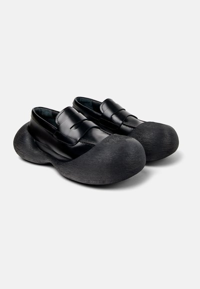 Scarpe nere con tomaia in pelle lucida e suola in gomma spessa e texturizzata. Presentano una punta arrotondata e una chiusura a doppia cinghia.