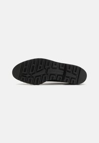 Suola di sneaker nera con un motivo di grip testurizzato, caratterizzata da profonde scanalature e accenti rialzati per una migliore aderenza e stabilità.