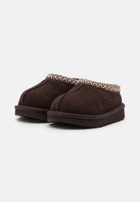 Chaussons en suède marron avec une couture texturée autour du col, semelles plates et bout arrondi. Design doux et confortable pour une utilisation intérieure.