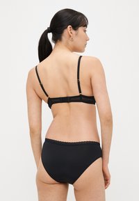 Set di lingerie nera con finitura liscia, spalline regolabili e dettaglio a bordi smerlati sulla fascia in vita. Design minimalista.