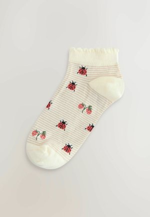 Bavlněná kotníková ponožka v krémové barvě s pruhovaným vzorem, zdobená motivy červené berušky a jahody. Volánkový lem přidává texturovaný detail.