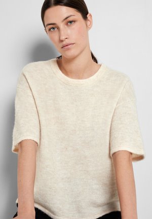 Pull en tricot de couleur crème avec des manches courtes et un col ras du cou, caractérisé par une texture douce et une coupe ample.