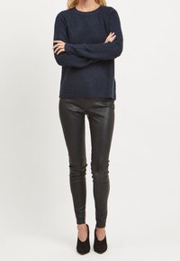 Pull en tricot côtelé marine avec col rond et fentes latérales, associé à des leggings en similicuir noir et des talons pointus noirs.