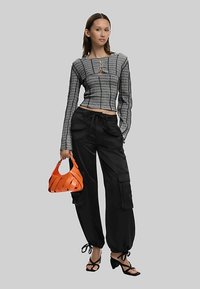 Black cargo pants with side pockets, fitted grey patterned long-sleeve top with a square cutout, and a bright orange woven handbag.