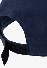 Navy plava kapa s kordurovom teksturom, zakrivljenim obodom i podesivim remenom s Velcro zatvaračem na stražnjoj strani.