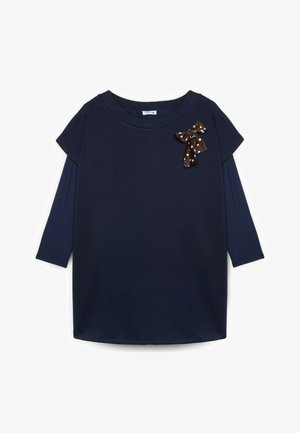 Marineblaues, langärmliges Kleid mit einer braunen Schleife mit Polka-Dots, die nahe am Ausschnitt auf der linken Seite befestigt ist.