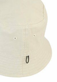 Beige bucket hat made from durable fabric, featuring a rounded crown, wide brim, and adjustable drawcord with black accents.